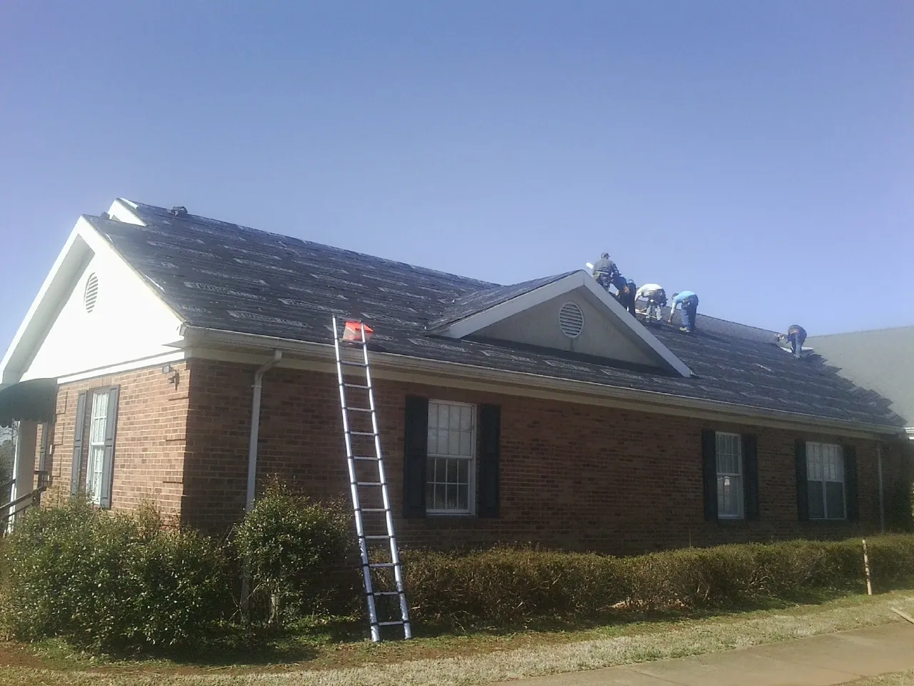 Crew tearing shingles off a brick ranch roof with a ladder set — Emergency Roof Repair work by our crew in Port Tobacco