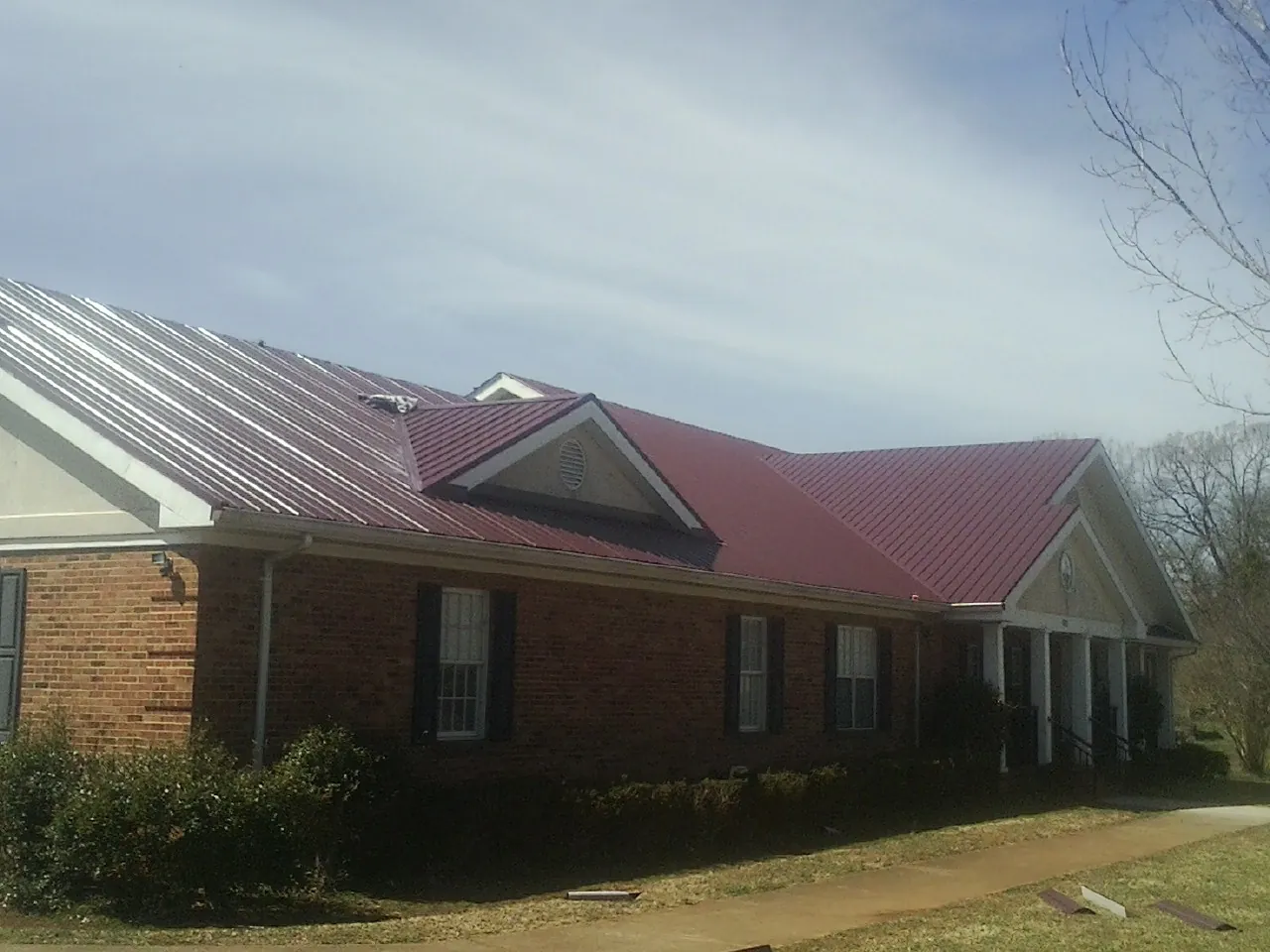 Red metal roof with gabled entries on a long brick building, from a Hail Damage Roof Repair job in Port Tobacco