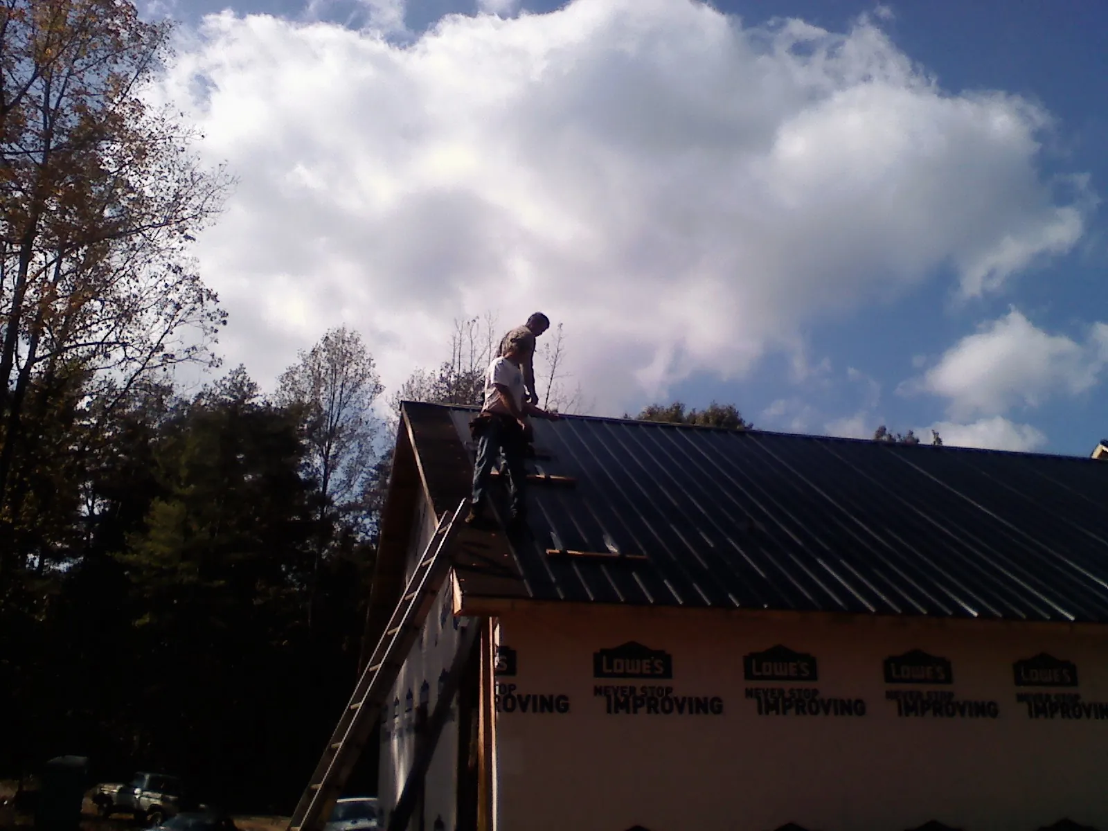Roofer fastening dark metal panels high against a cloudy sky, from a Roof Inspection job in Port Tobacco
