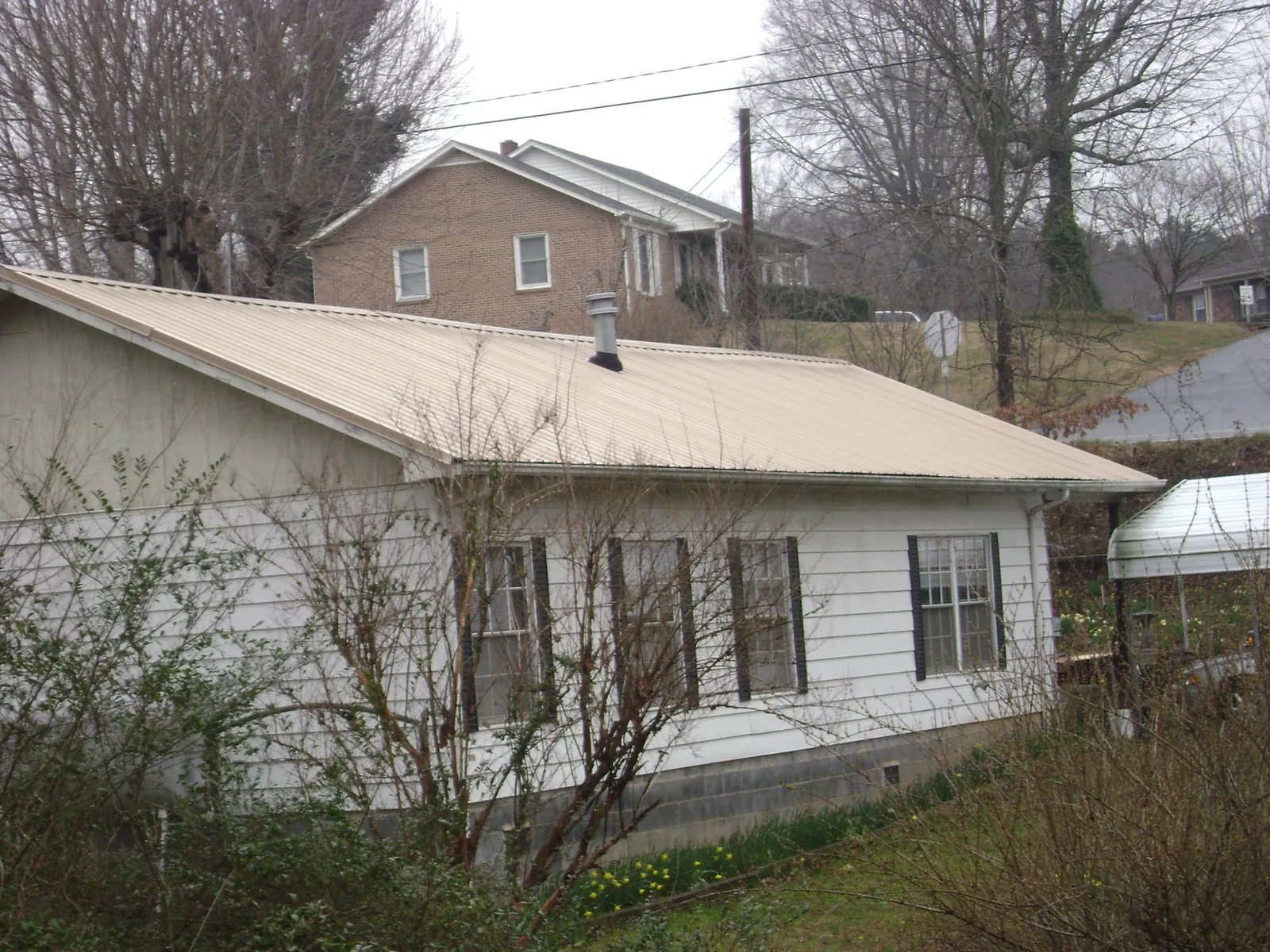 Tan metal roof on a white sided house set into a hillside — Commercial Roofing by Roofing Brothers in Port Tobacco